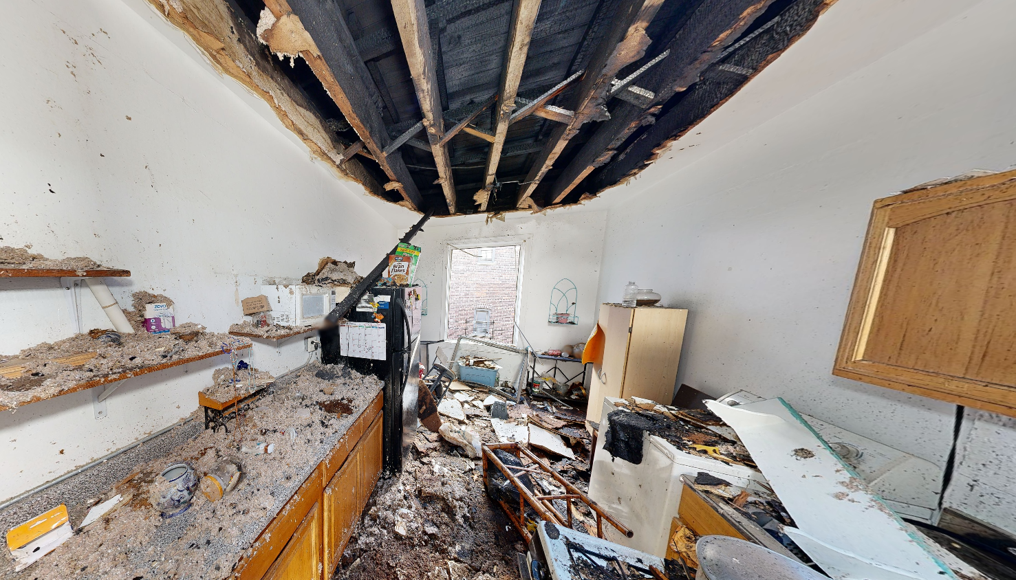 Kitchen fire damage showing extensive ceiling collapse with exposed burned structural beams and debris